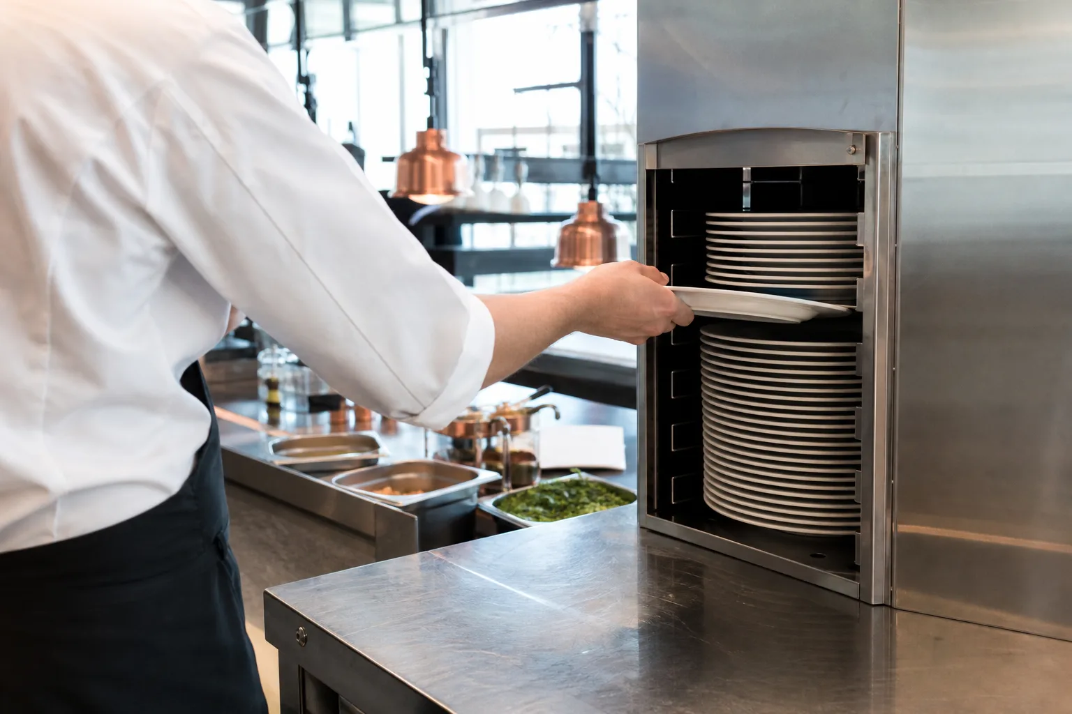 Rostfri tallriksvärmare vid uppläggningen i ett restaurangkök med en trave varma tallrikar